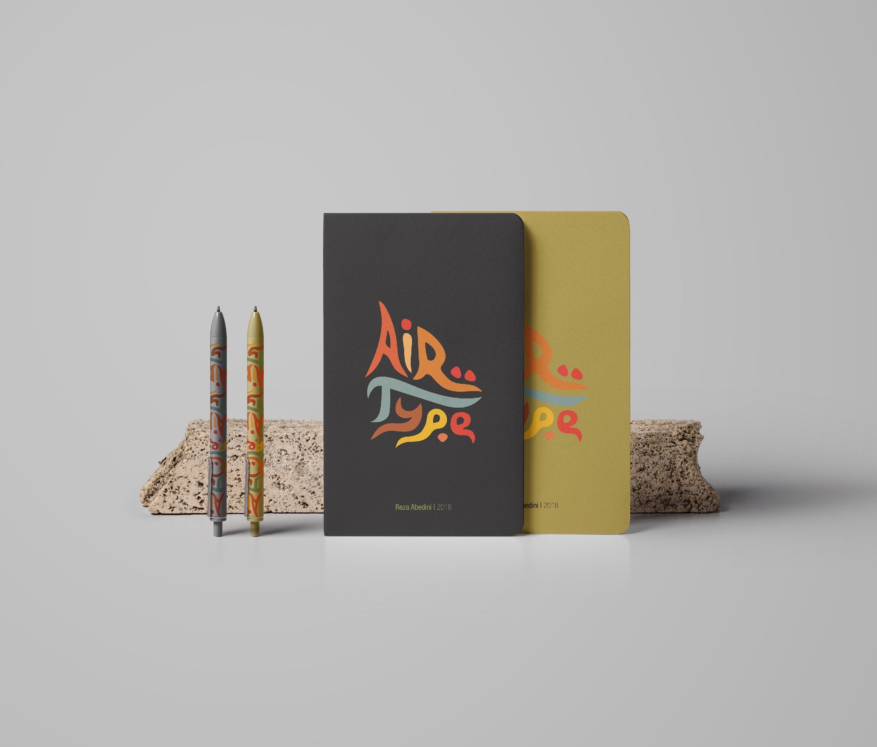 The merchandise: a black notebook and a yellow notebook standing on a stone block with the logo across the cover, and two pencils printed with the same lettering