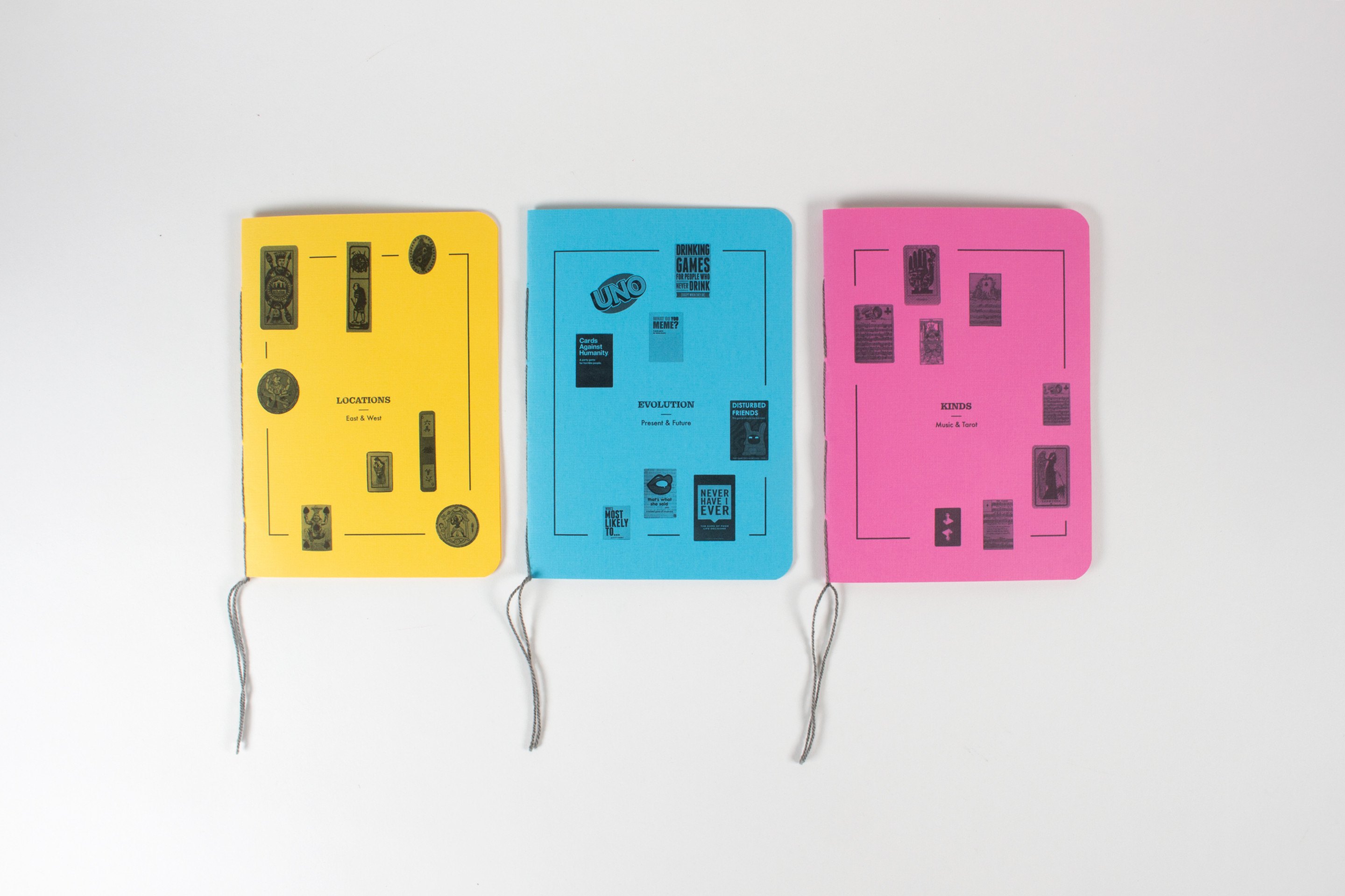 The three books laid out side by side: a yellow, a blue and a magenta cover, each printed with a card-back diagram and tied with a grey thread