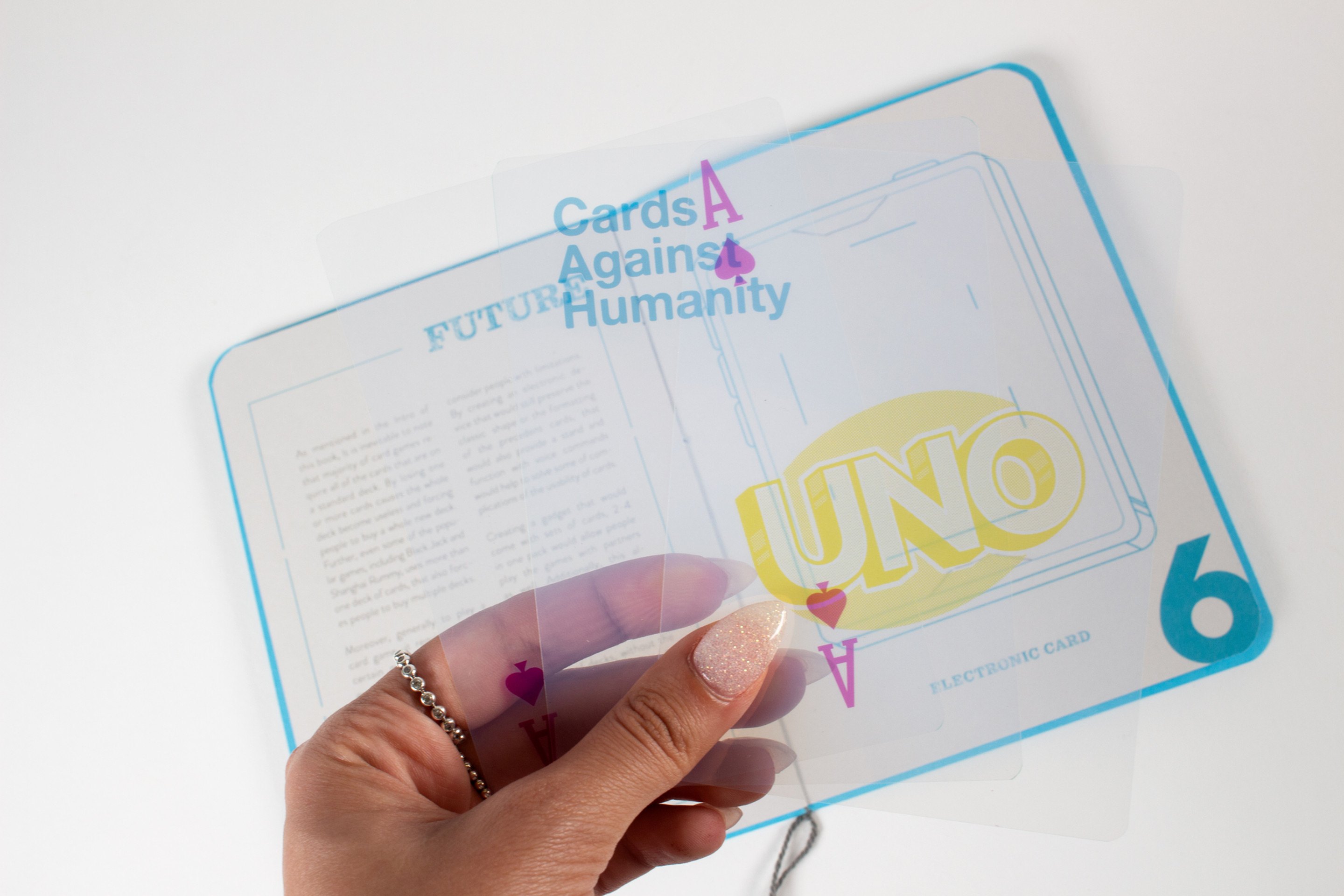 A hand holding a printed transparent card over the same Future spread, a Cards Against Humanity card overlaying the UNO drawing beneath