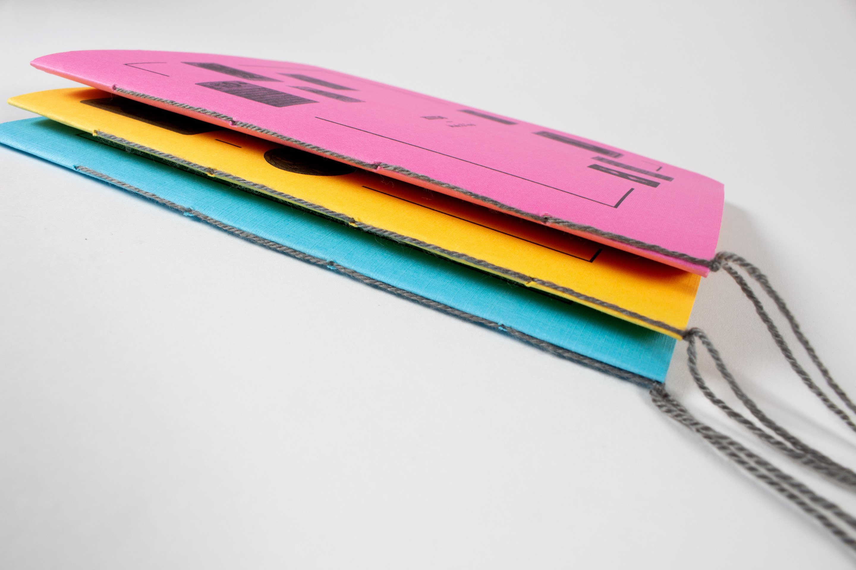 All three books stacked flat and slightly offset so the yellow, magenta and blue edges step across the frame