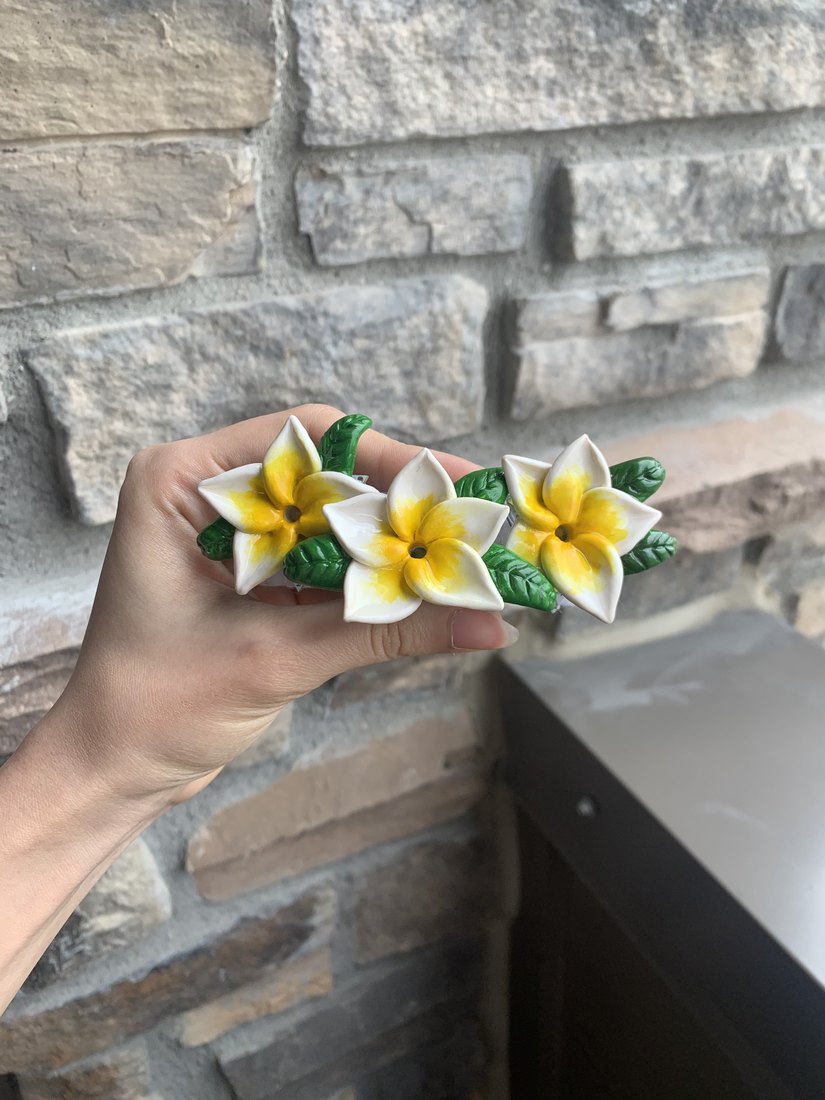 The frangipani hair clip held up to a stone wall