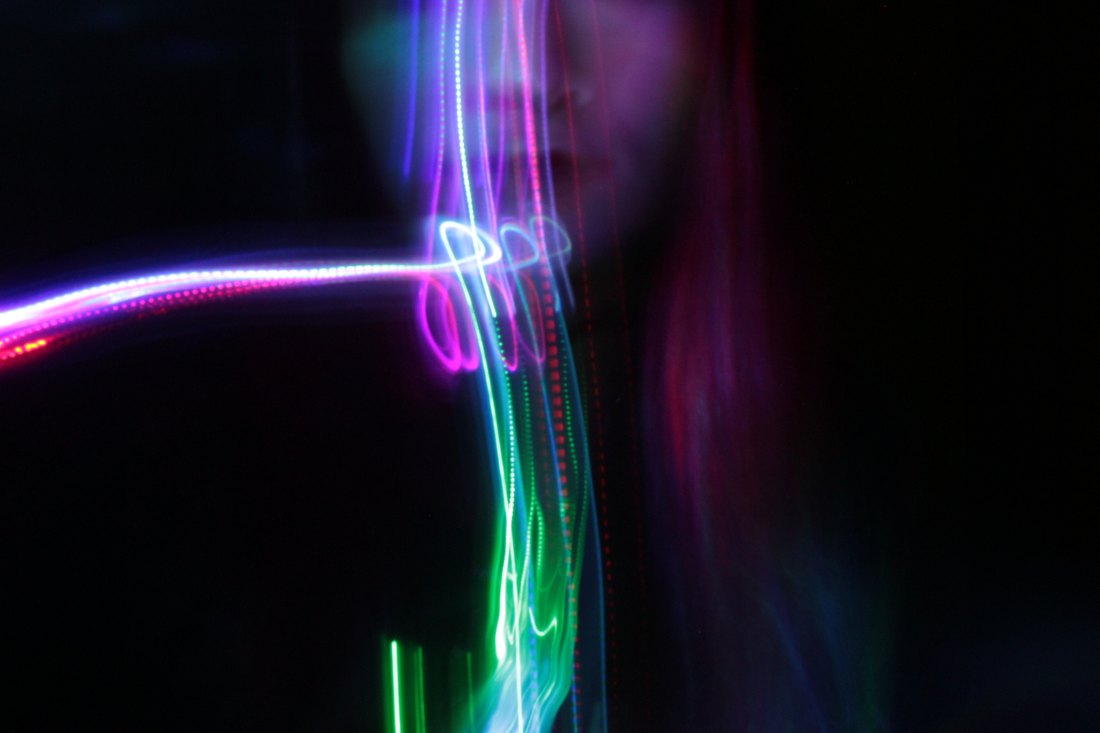 Light trails looping across a figure in the dark, pink and green