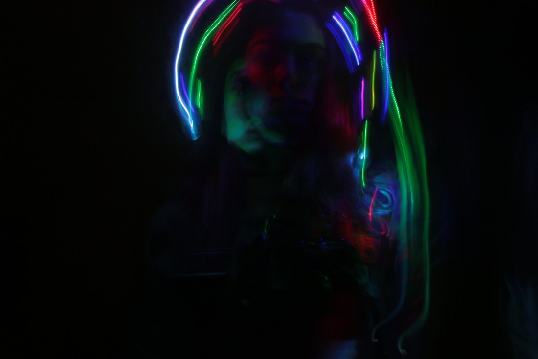 A figure lit by red and blue trails, hair caught in the light
