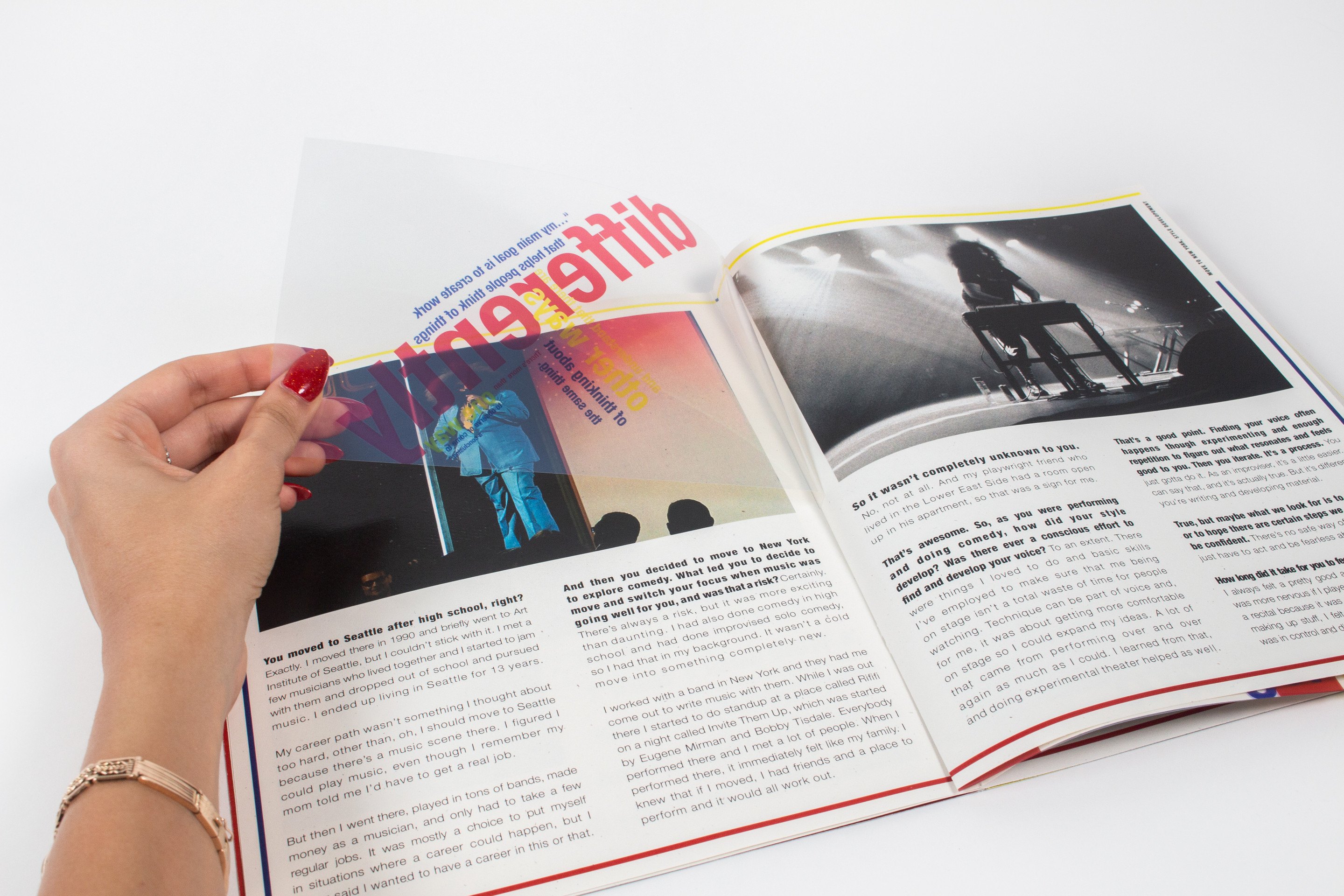 Hands lifting a printed transparent sheet away from a spread, the word “differently” in red and blue coming off the page beneath