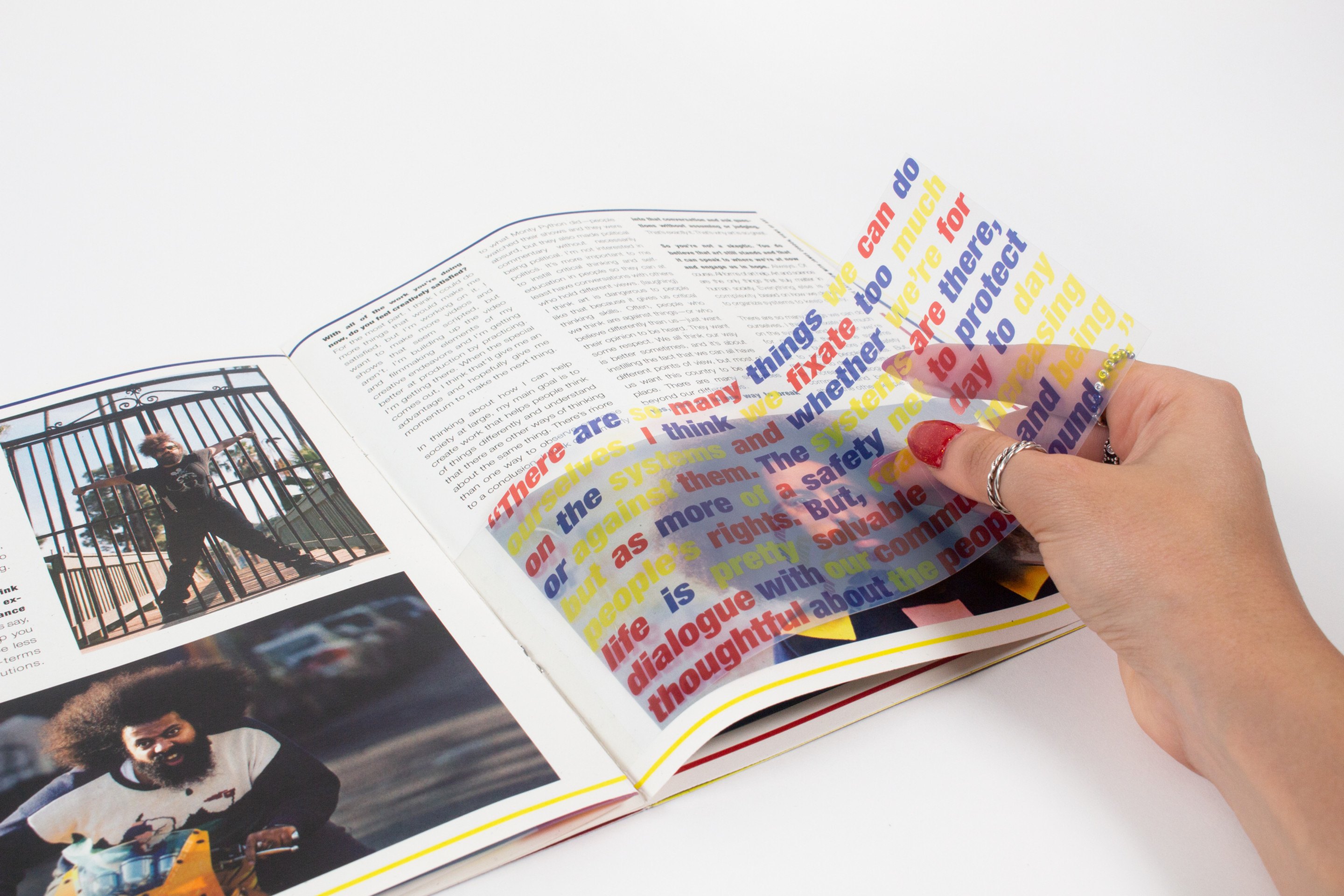 Hands holding several transparent sheets fanned open at once above a spread, layers of red, blue and yellow type overlapping