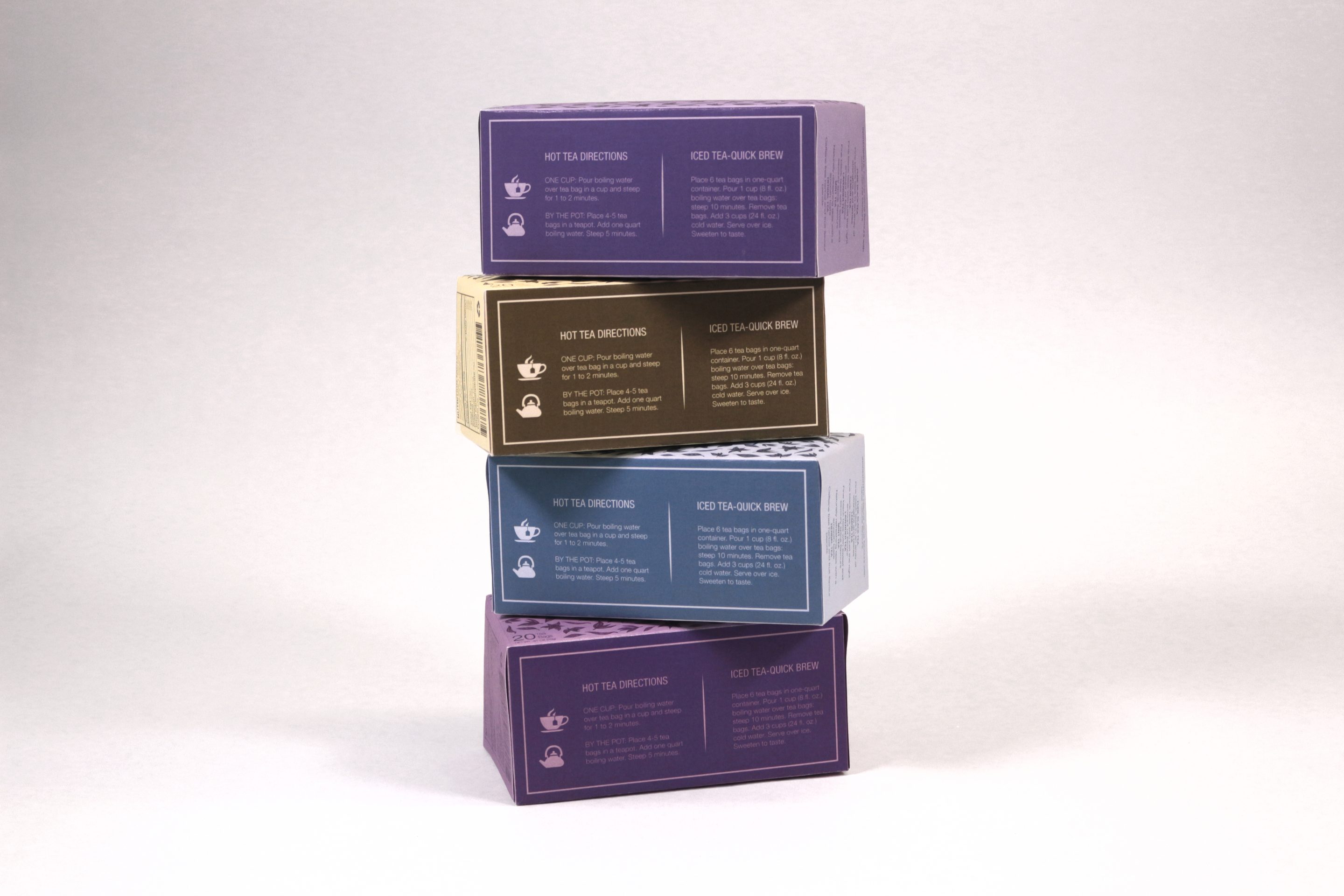 The four boxes stacked and staggered, back panels out, each carrying its hot tea directions and an iced tea quick brew beside them