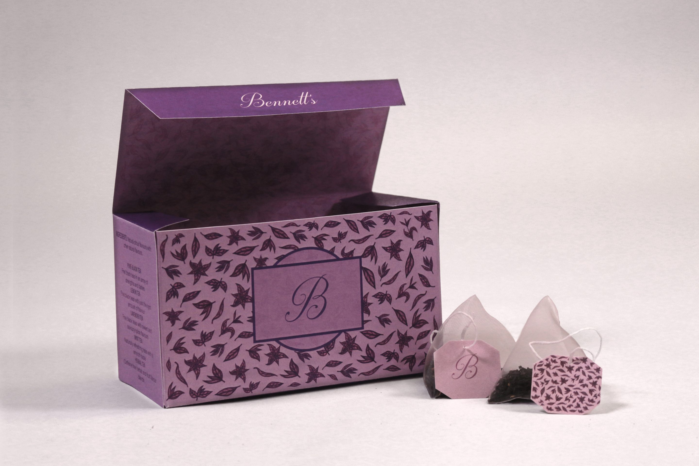 One box open in mauve, the lid folded back to show the printed lining, with three pyramid tea bags and their patterned tags beside it