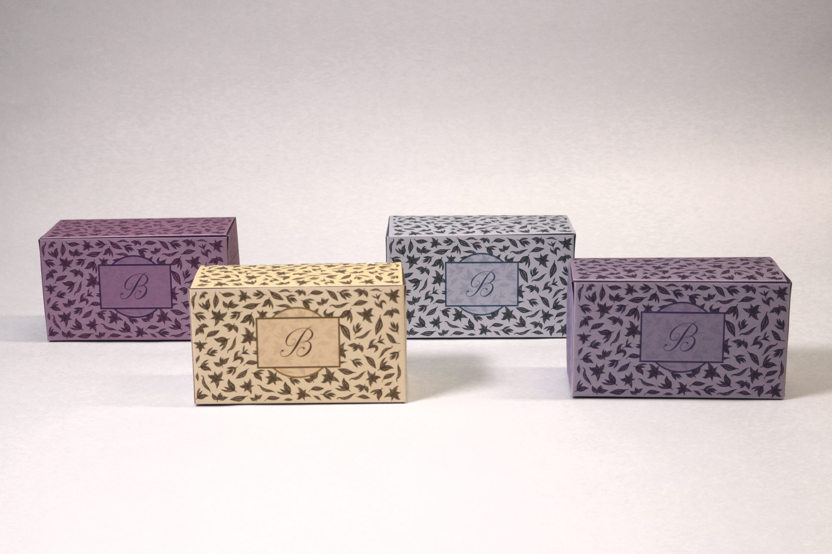 The same four boxes set apart on a pale ground, each turned to show the monogrammed B panel on its front