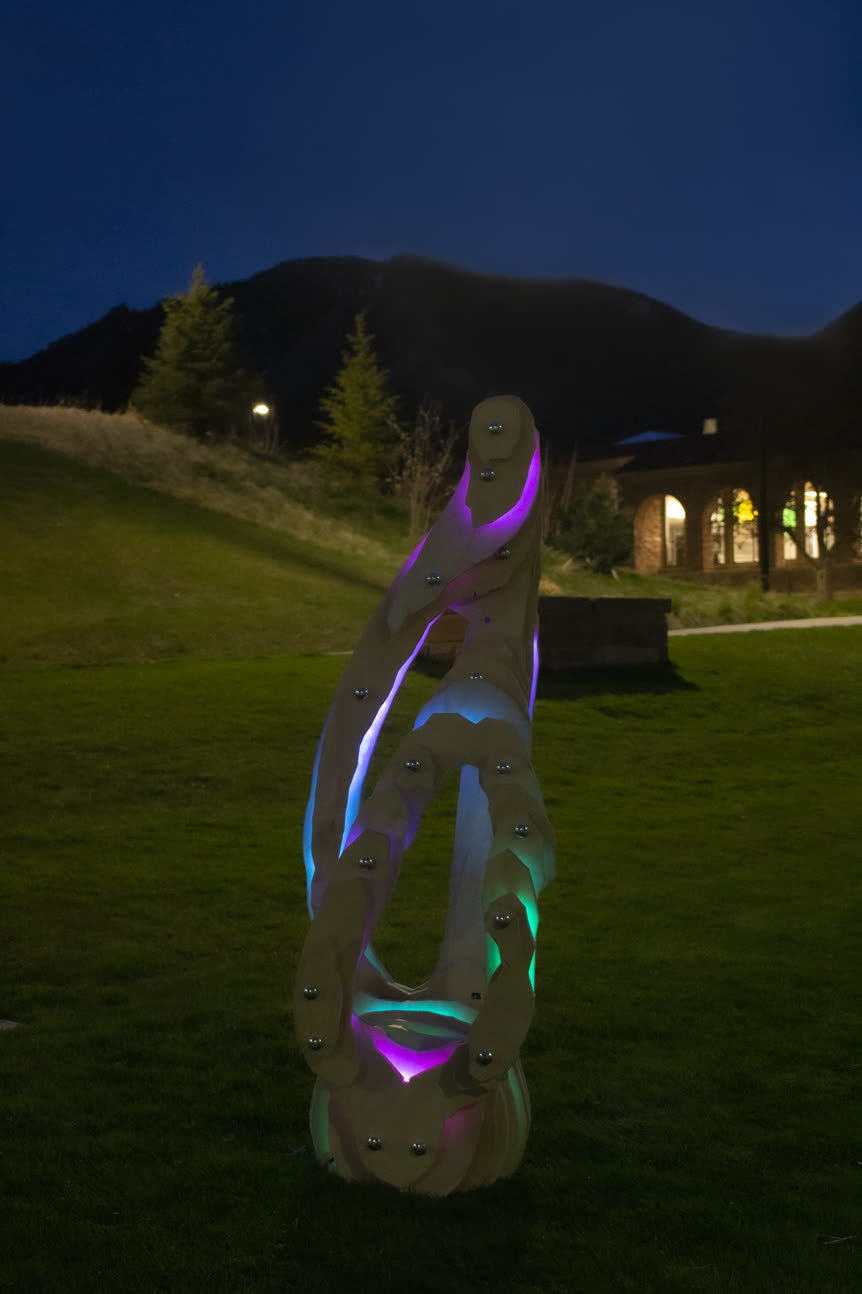 Zora standing on grass at dusk, lit teal and violet, with a mountain and a lit building behind it.